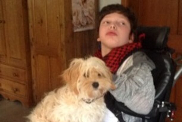 Male teenager sitting in an electric wheelchair with a medium sized terrier dog on his lap