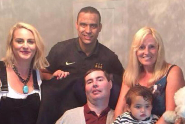 Happy family of three generations, standing around a middle aged male in a wheelchair
