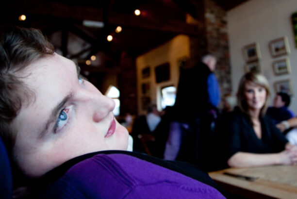 Teenager with disability in the foreground in a restaurant with family and friends in the background