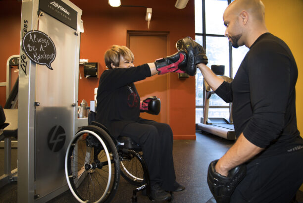 Woman in a wheelchair at the gym boxing with a male partner who is kneeling down